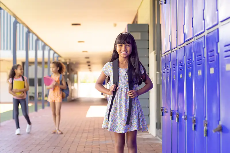 Young girl, with a backpack standing in front of her school locker